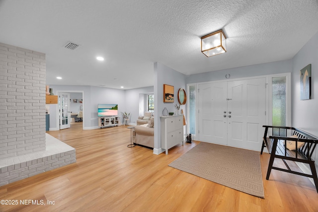 entryway featuring baseboards, visible vents, a textured ceiling, light wood-type flooring, and recessed lighting