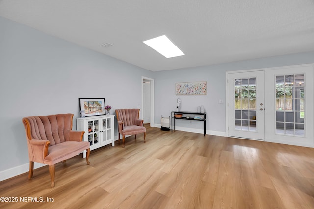 living area featuring light wood finished floors, baseboards, visible vents, and a textured ceiling