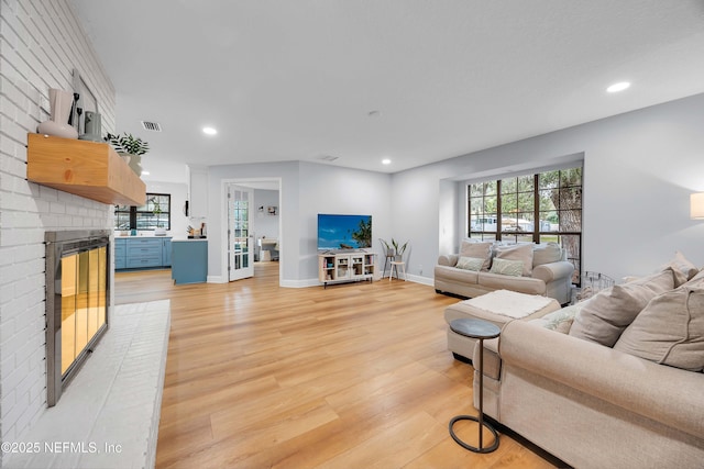 living room with visible vents, a brick fireplace, and light wood-style flooring