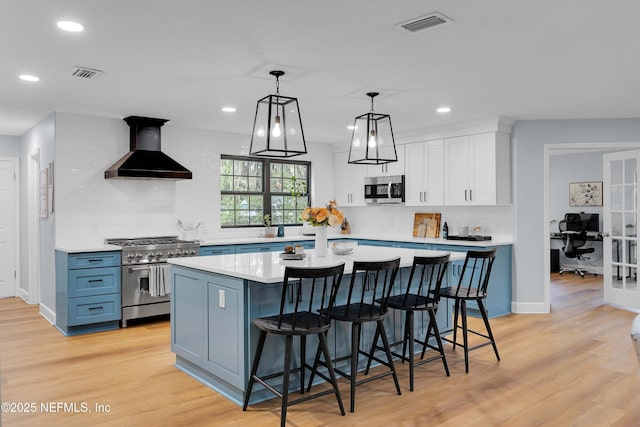 kitchen with appliances with stainless steel finishes, light countertops, blue cabinetry, premium range hood, and white cabinetry