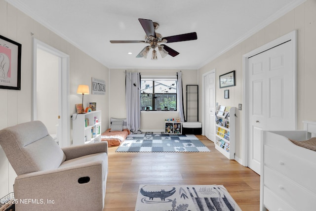 living area featuring ceiling fan, light wood-style flooring, and crown molding