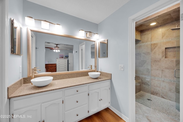 bathroom featuring ceiling fan, double vanity, a sink, and a shower stall