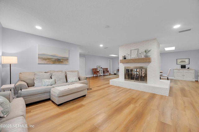 living room with recessed lighting, light wood-type flooring, visible vents, and a brick fireplace