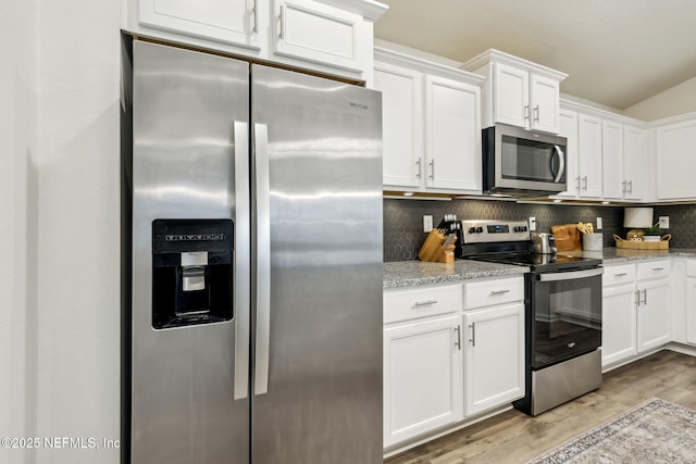 kitchen with light wood finished floors, white cabinets, appliances with stainless steel finishes, light stone countertops, and backsplash