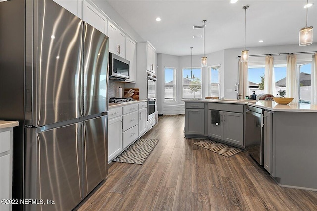 kitchen with gray cabinets, appliances with stainless steel finishes, white cabinetry, hanging light fixtures, and dark hardwood / wood-style flooring