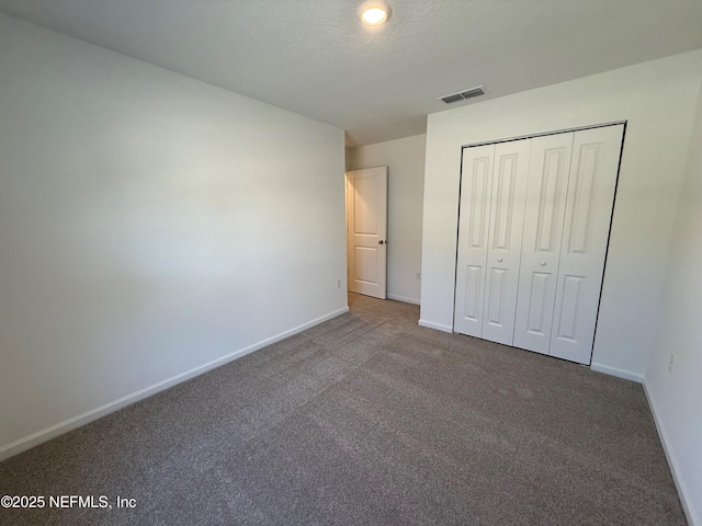 unfurnished bedroom with visible vents, a textured ceiling, a closet, carpet, and baseboards