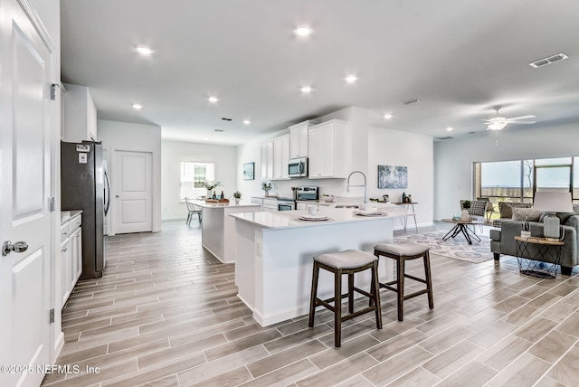 kitchen with a peninsula, a kitchen island, light countertops, appliances with stainless steel finishes, and wood tiled floor