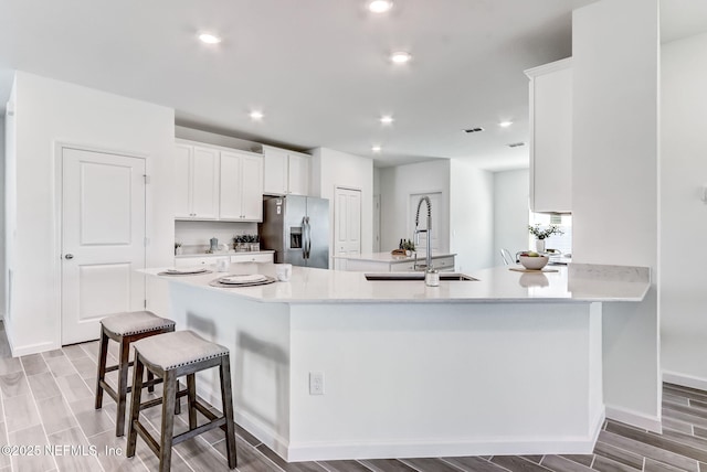 kitchen featuring a breakfast bar, light countertops, white cabinets, a sink, and stainless steel fridge with ice dispenser