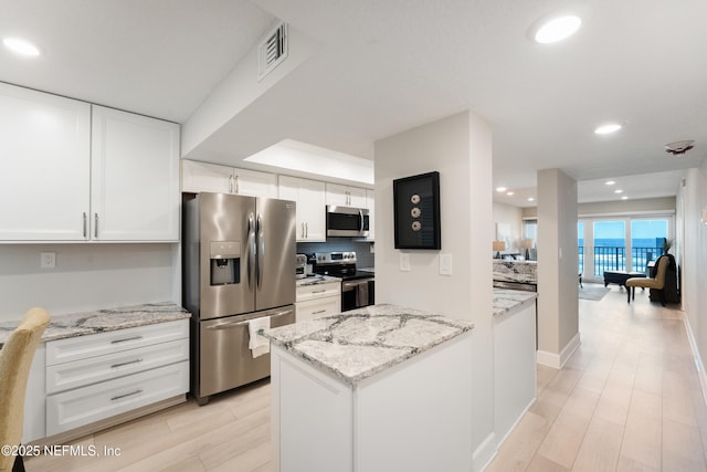 kitchen featuring appliances with stainless steel finishes, light wood-style flooring, decorative backsplash, white cabinetry, and light stone counters