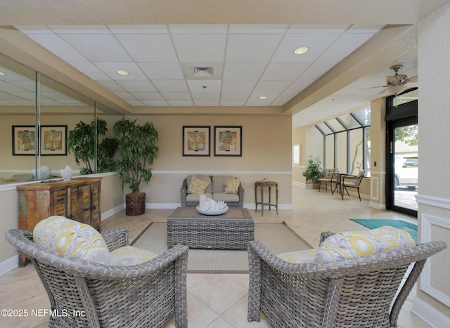 living area featuring visible vents, a ceiling fan, a drop ceiling, baseboards, and light tile patterned flooring