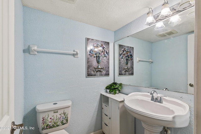 half bathroom featuring visible vents, a textured wall, toilet, a textured ceiling, and a sink