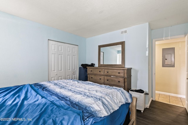 bedroom with a closet, visible vents, a textured ceiling, wood finished floors, and electric panel