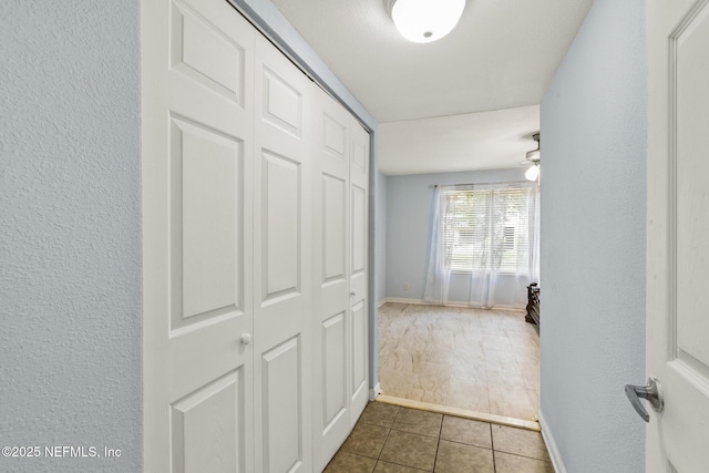 hallway with a textured wall, tile patterned floors, and baseboards