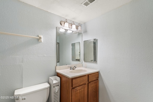 bathroom with visible vents, a textured wall, vanity, and toilet