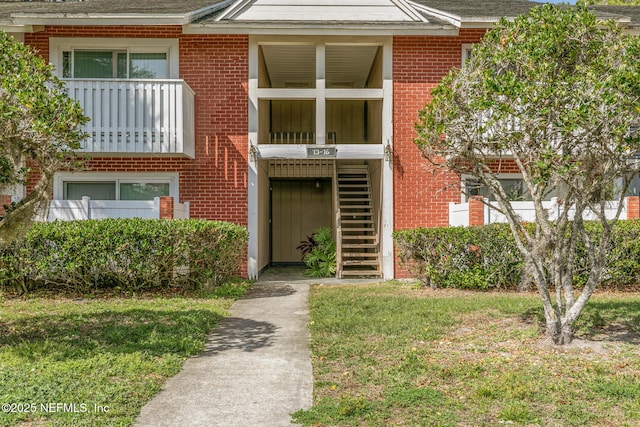 view of front of home with a front yard, brick siding, and stairs