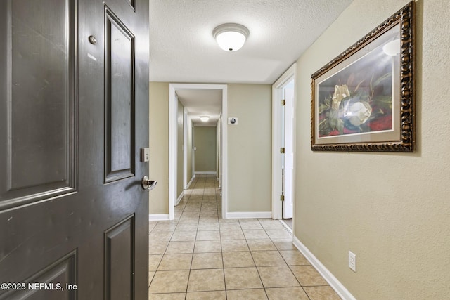 hallway with light tile patterned floors, baseboards, and a textured ceiling