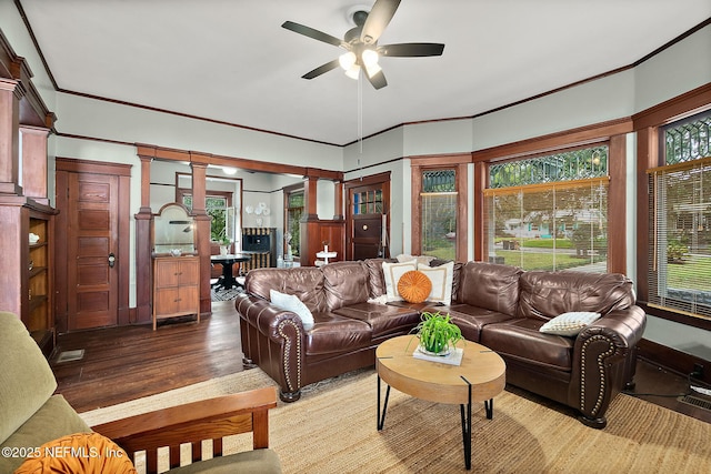 living area with decorative columns, crown molding, ceiling fan, and wood finished floors