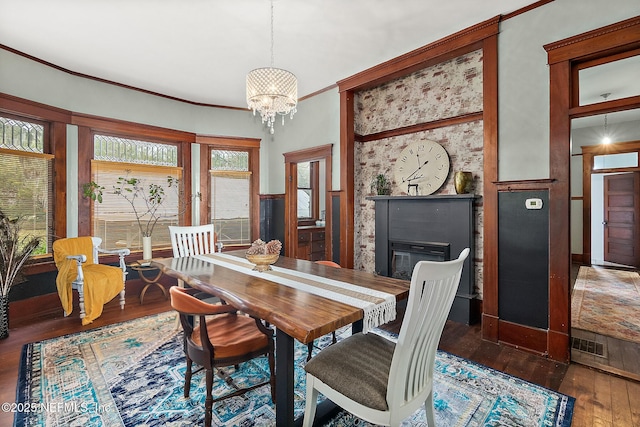 dining room featuring visible vents, ornamental molding, wood-type flooring, a glass covered fireplace, and an inviting chandelier