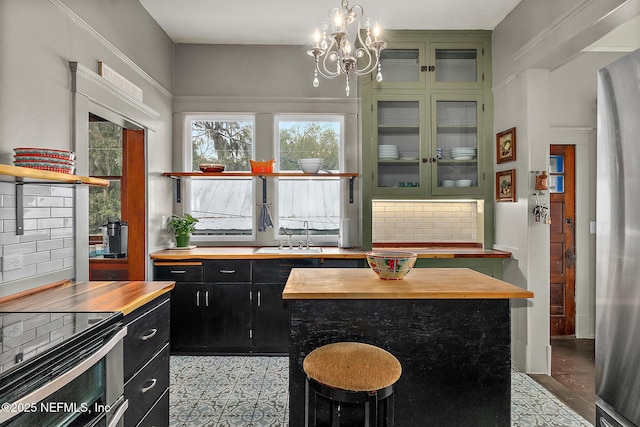 kitchen with tasteful backsplash, freestanding refrigerator, a sink, butcher block countertops, and dark cabinetry