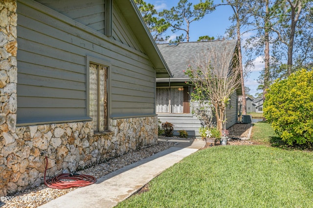 view of property exterior featuring stone siding, central AC unit, a lawn, and roof with shingles