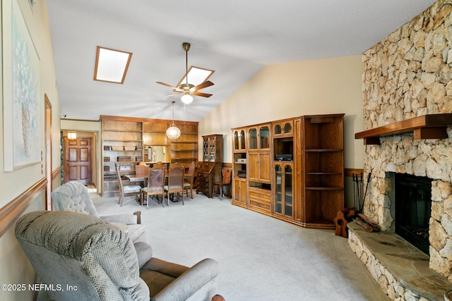 carpeted living room featuring vaulted ceiling with skylight, a stone fireplace, and a ceiling fan