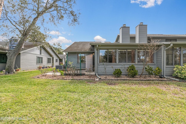 back of property featuring a sunroom, a chimney, central AC, and a lawn