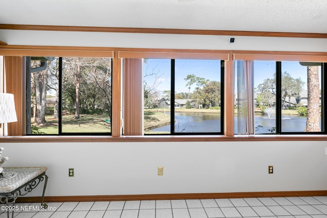 unfurnished room with a textured ceiling, light tile patterned floors, a water view, and baseboards