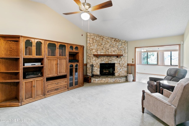 living area with high vaulted ceiling, light colored carpet, ceiling fan, and a stone fireplace