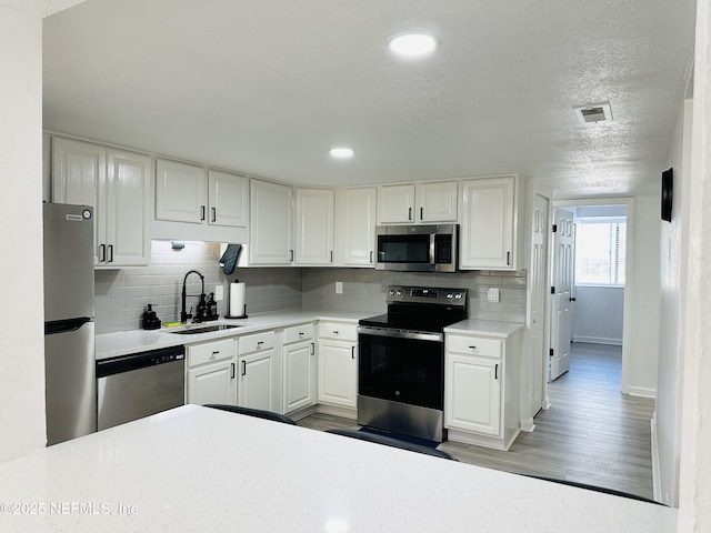 kitchen featuring sink, appliances with stainless steel finishes, hardwood / wood-style floors, white cabinets, and decorative backsplash