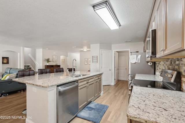 kitchen featuring appliances with stainless steel finishes, a breakfast bar, sink, a kitchen island with sink, and light stone countertops