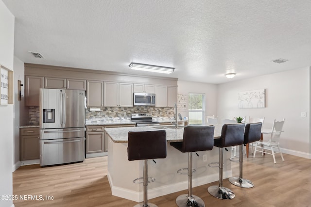 kitchen with sink, gray cabinets, stainless steel appliances, light stone countertops, and an island with sink