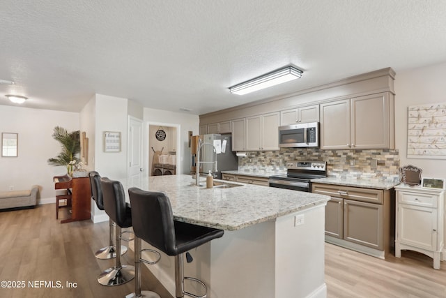 kitchen featuring light stone counters, sink, stainless steel appliances, and a center island with sink