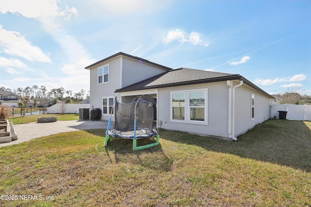 back of property with a patio, a lawn, a trampoline, and an outdoor fire pit