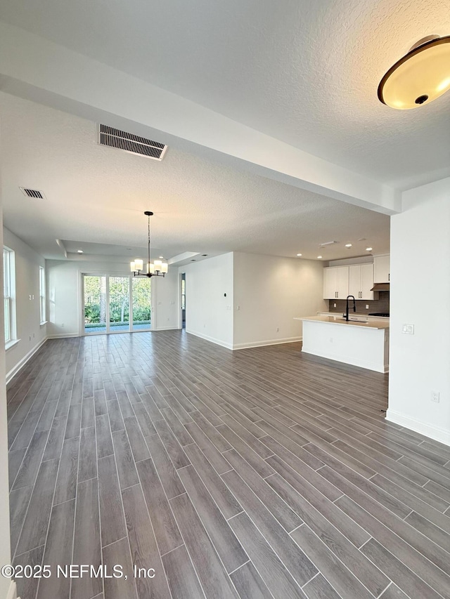 unfurnished living room featuring a notable chandelier, visible vents, a sink, and wood finish floors