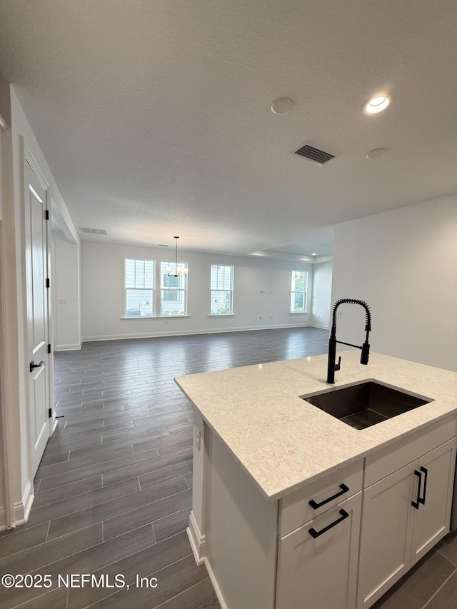 kitchen featuring visible vents, open floor plan, white cabinets, a sink, and an island with sink