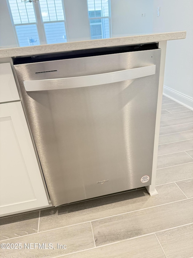 interior details with baseboards, white cabinets, dishwasher, wood tiled floor, and light countertops