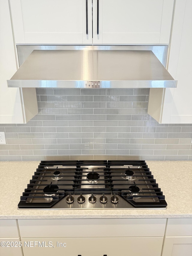 details featuring white cabinets, decorative backsplash, light countertops, wall chimney range hood, and gas cooktop