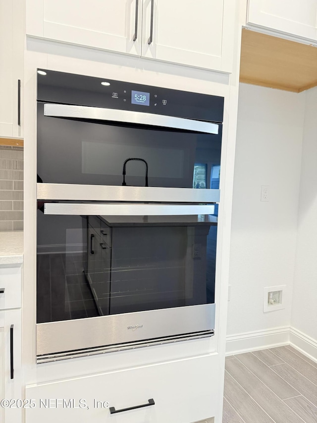 interior details with tasteful backsplash, baseboards, light countertops, stainless steel double oven, and white cabinetry