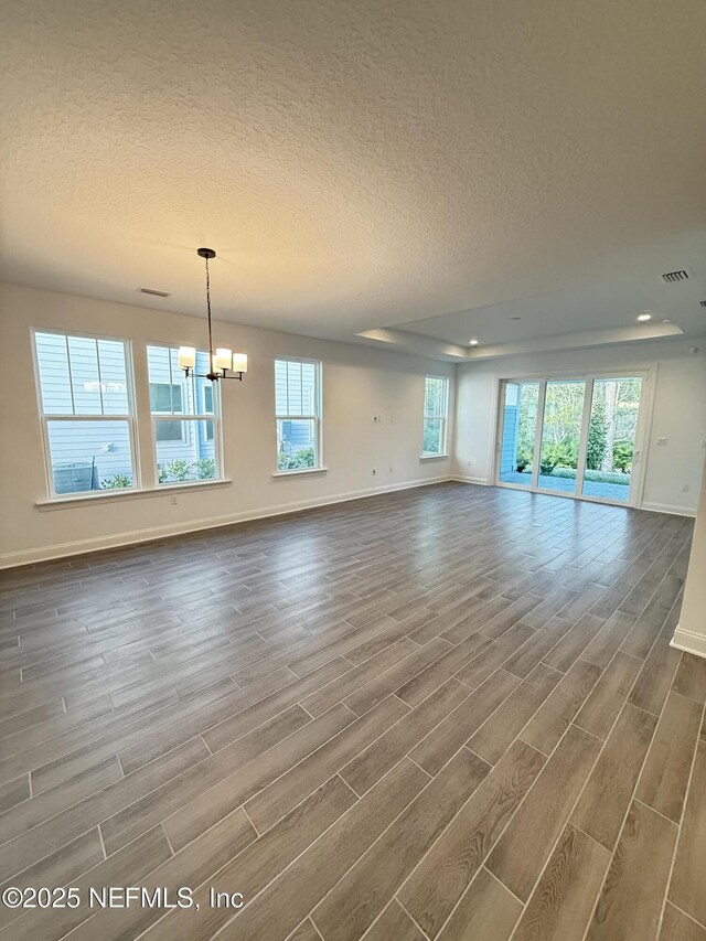 unfurnished living room with wood tiled floor, a notable chandelier, a textured ceiling, and baseboards