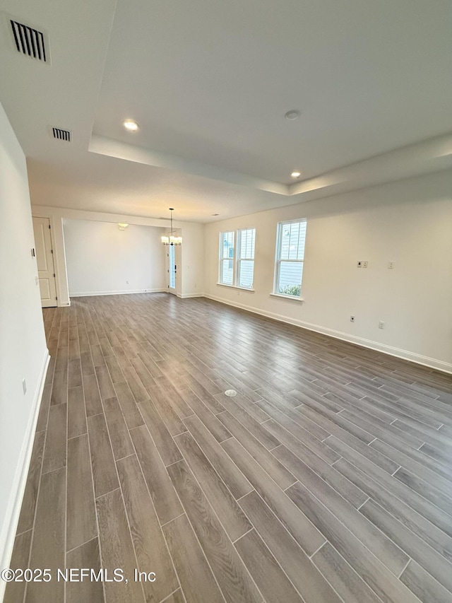 unfurnished living room with a tray ceiling, dark wood finished floors, visible vents, and baseboards