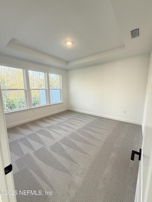 carpeted spare room featuring a raised ceiling, visible vents, and baseboards