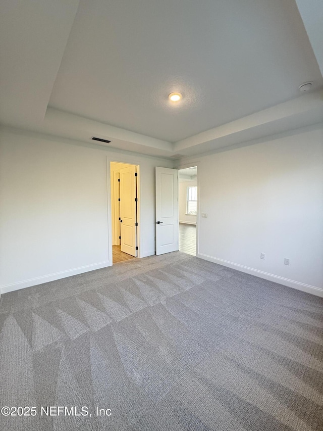 unfurnished bedroom with light carpet, baseboards, visible vents, and a tray ceiling