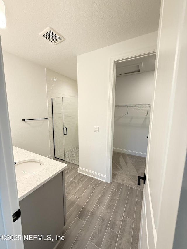 bathroom with visible vents, wood tiled floor, a spacious closet, vanity, and a shower stall