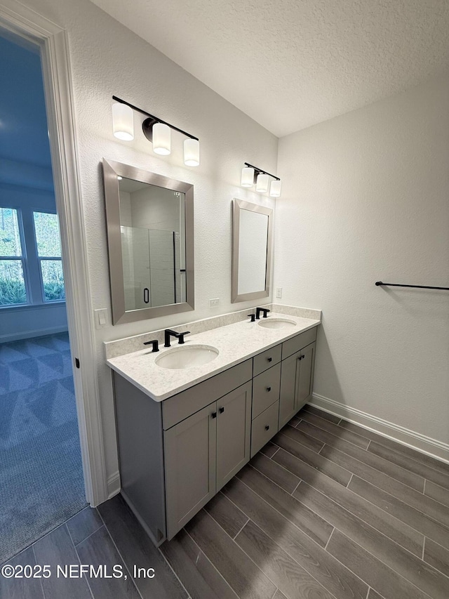 bathroom with wood tiled floor, a sink, a textured ceiling, and double vanity