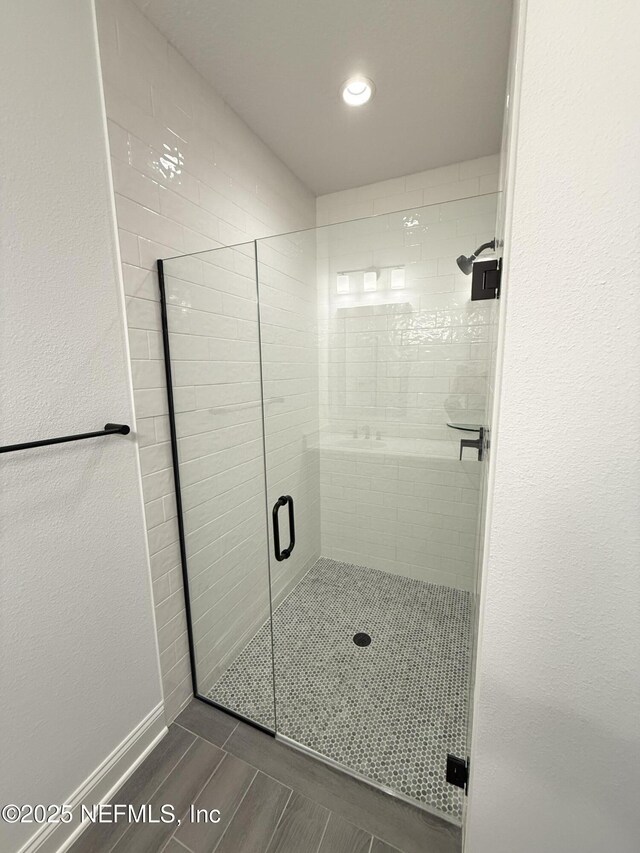 bathroom featuring a textured wall, a shower stall, and baseboards