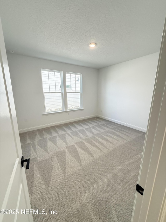 unfurnished room with light carpet, a textured ceiling, and baseboards