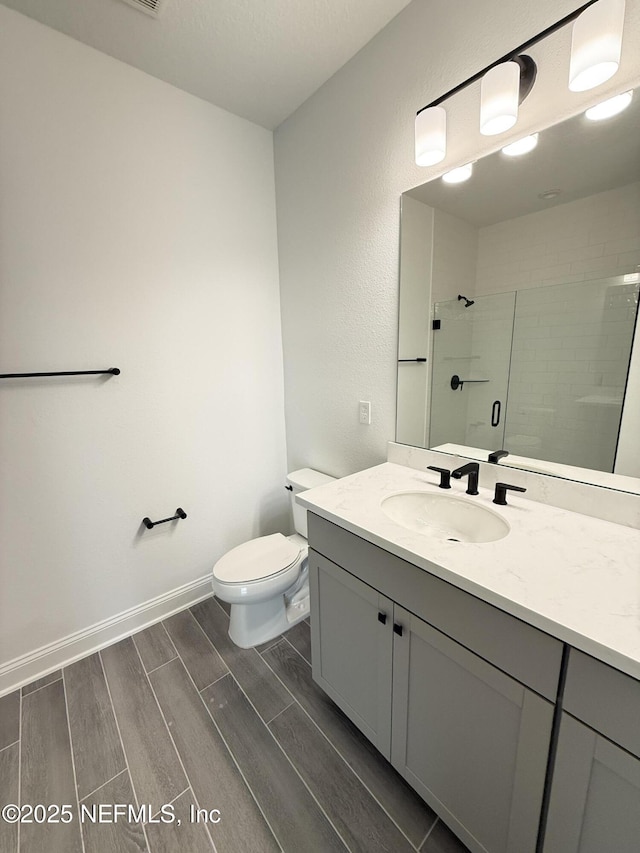 full bath featuring toilet, wood finish floors, vanity, baseboards, and a tile shower