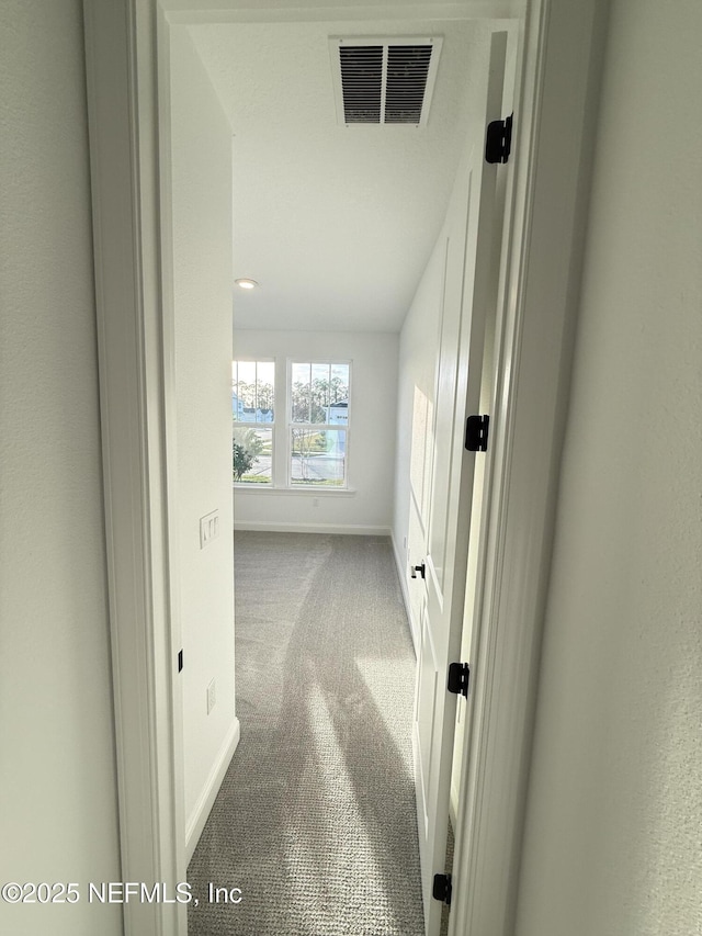 corridor with baseboards, visible vents, and carpet flooring