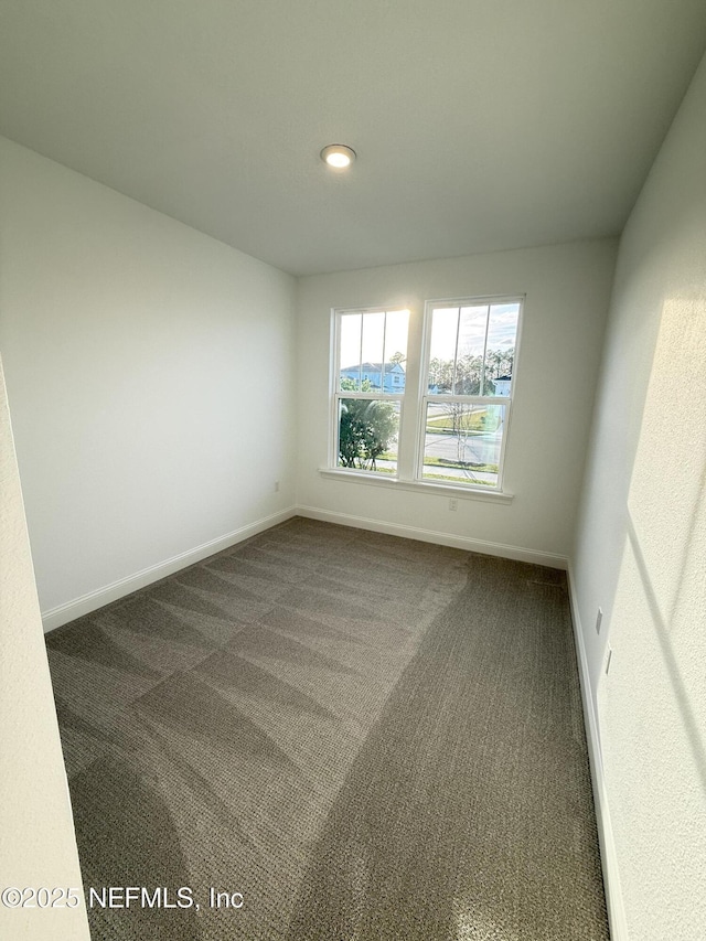 spare room featuring dark carpet and baseboards