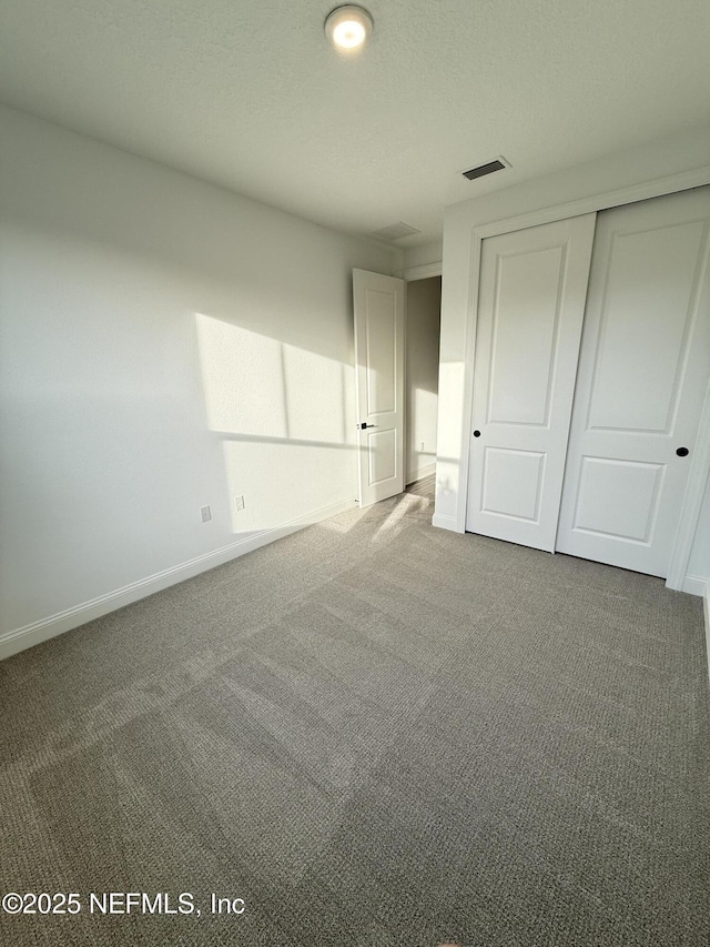 unfurnished bedroom featuring baseboards, visible vents, a textured ceiling, dark carpet, and a closet